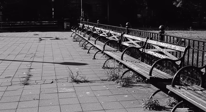 A gritty, black and white depiction of Tompkins Square Park in the 1980s, looking run-down and neglected, suggesting its dangerous reputation before revitalization.